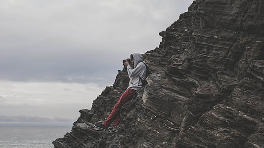 person holding DSLR camera taking a photo while standing on brown rock thumbnail
