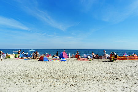 people standing and sitting on shore near sea at daytime thumbnail