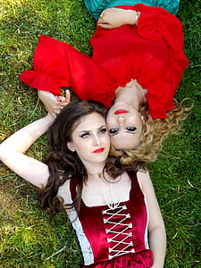 woman in maroon dress beside woman in red top lying on green grass thumbnail