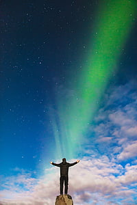 man standing on brown rock formation under Aurora Borealis during daytime thumbnail