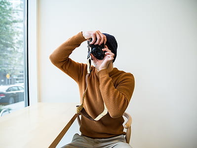 man wearing brown sweater holding black DSLR camera thumbnail