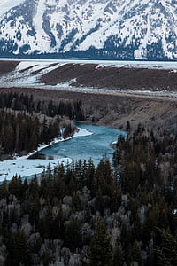rippling body of water surrounded with trees and alp mountains covered with snow thumbnail