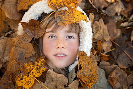 flat lay photography of girl wearing white and gray fur jacket lying on brown leaves thumbnail