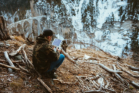 man sitting on cliff while holding iPad thumbnail