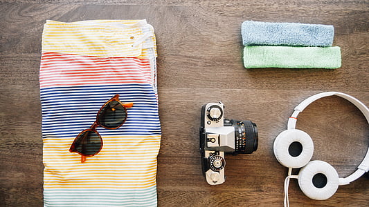 flat lay photography of camera, headphones, sunglasses, and board shorts thumbnail