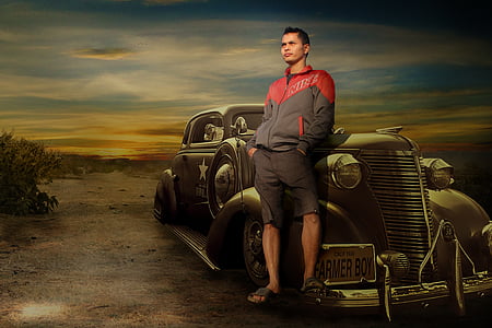man wearing red and black full-zip jacket and black shorts leaning on black car thumbnail