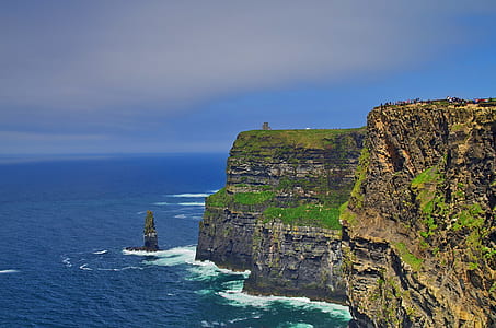 brown and green rock cliff surrounded by body of water during daytime thumbnail