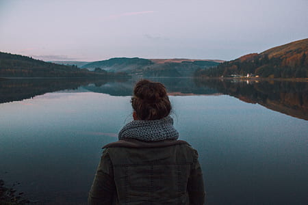 person wearing brown jacket facing towards calm water thumbnail