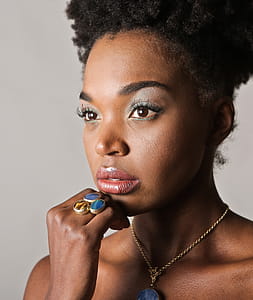 A young African woman wearing jewelry posing indoors with her fingers on her chin thumbnail