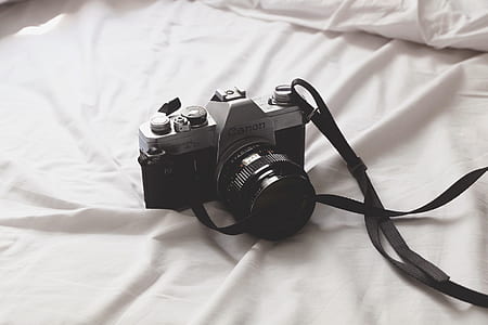black and gray Canon DSLR camera on white textile thumbnail