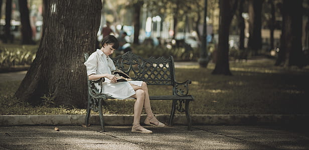 Woman Sitting on Metal Bench on Park While Reading Book thumbnail