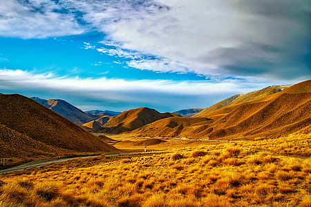 field of brown grass beside mountain under blue sky thumbnail