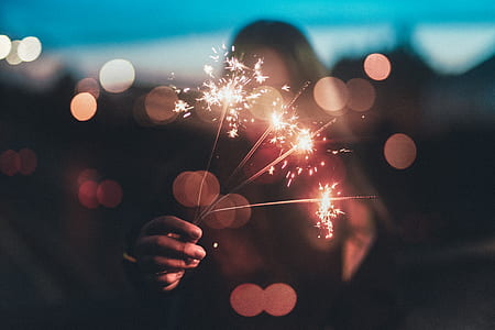 bokeh photography of a person holding sparklers during nighttime thumbnail