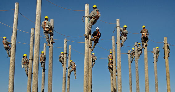 group of men wearing gray and black coveralls climbing electrical post during daytime thumbnail