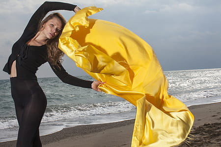 woman holding yellow textile standing in front of seashore thumbnail