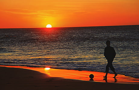 silhouette of man walking on shore with ball during sunset thumbnail
