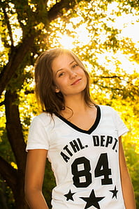woman wearing white and black V-neck t-shirt standing near tree during daytime thumbnail