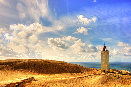 gray lighthouse on brown sand during blue cloudy day thumbnail