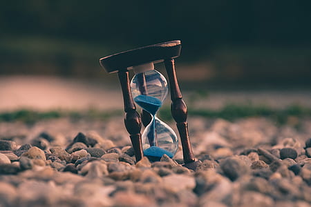 focused photography of hourglass on gray stones thumbnail