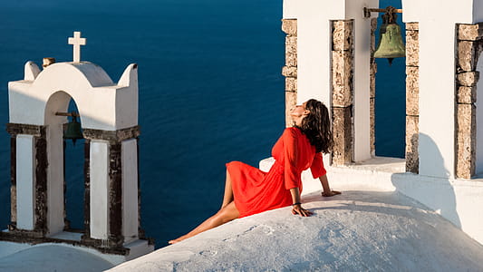 Woman in Red Long-sleeved Dress Sitting On White Concrete Building thumbnail