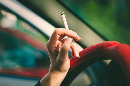 person holding cigarette stick leaning on steering wheel thumbnail