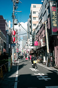woman riding bike on road between buildings thumbnail