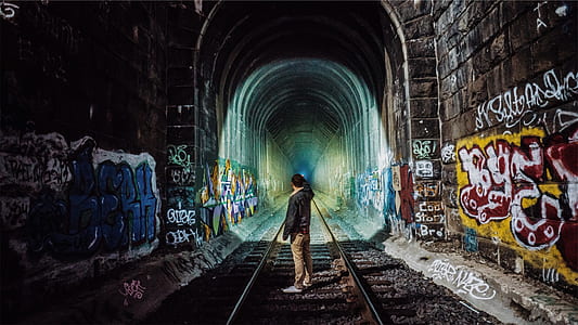 man standing in middle of train track tunnel thumbnail