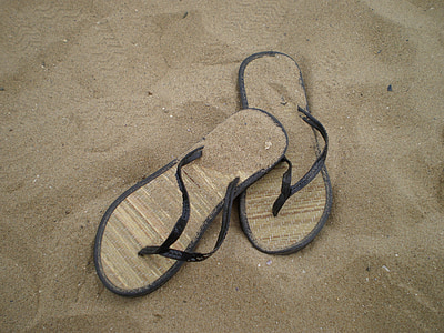 pair of black-and-brown flip-flops on brown sand thumbnail