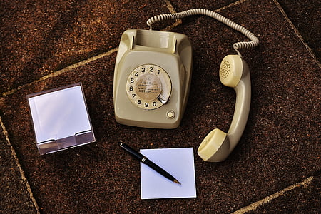 beige rotary telephone beside white paper and retractable pen thumbnail