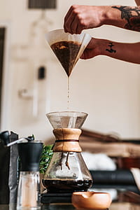 person holding filled coffee filter while pouring clear glass container thumbnail