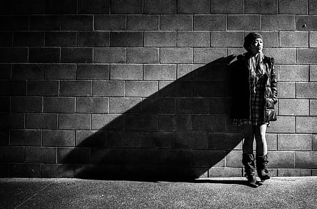 grayscale photography of woman leaning on brick wall wearing jacket and booties thumbnail
