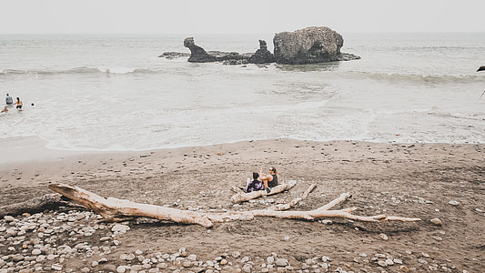 man and woman sitting on sand in front of sea thumbnail