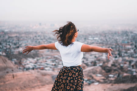 woman standing on cliff while raising her hands sideward during daytime thumbnail