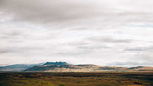 Panoramic view of gray cloudy sky over the vast field with mountains in the background thumbnail