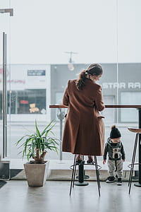 woman in brown coat sits beside boy standing thumbnail