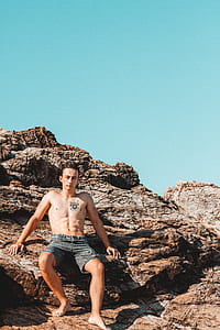 man in black denim shorts sitting on rock formation thumbnail