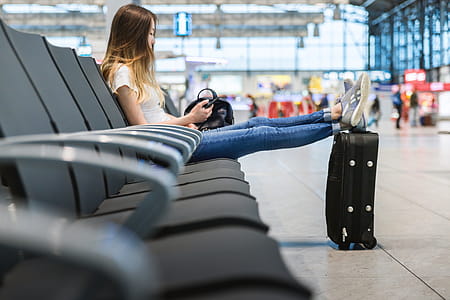 Young girl with long hair is sitting in airport. She put her legs on suitcase near. thumbnail