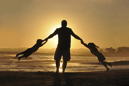silhouette photo of a man swinging two children using his hands near the shore thumbnail