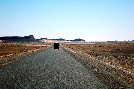 black SUV running on road surrounded by desert during day thumbnail