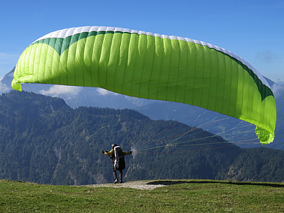 person standing on hill while using paracliding under blue sky thumbnail