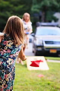 Girl Wearing Multicolored Floral Sleeveless Dress Throwing Red Handkerchief Standing on Green Grass during Daytie thumbnail