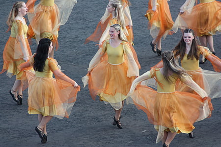 group of women wearing yellow and orange dresses dancing together thumbnail