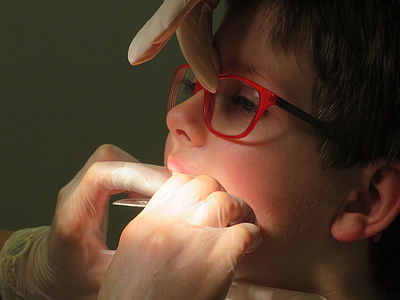 dentist checks teeth of boy with red eyeglasses thumbnail