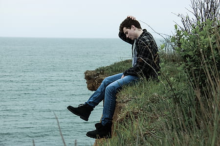 man sitting in the edge of mountain surrounded by grass thumbnail