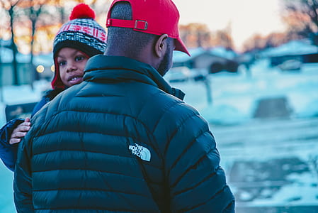 man in black The North Face jacket carrying child on street thumbnail
