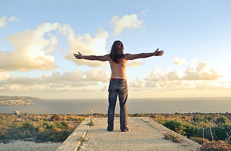A man wearing a denim jeans standing on a seashore with his arms stertched thumbnail