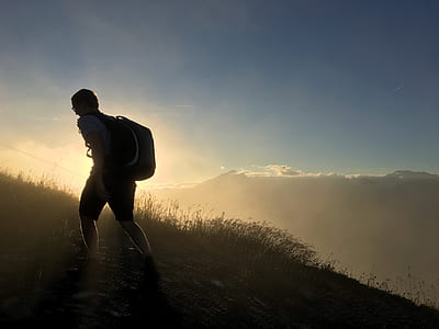 silhouette photo of man with backpack standing grass covered ground thumbnail
