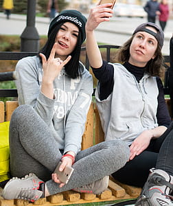 Woman Holding Smartphone While Taking Selfie Beside Woman Wearing Black Knit Cap thumbnail