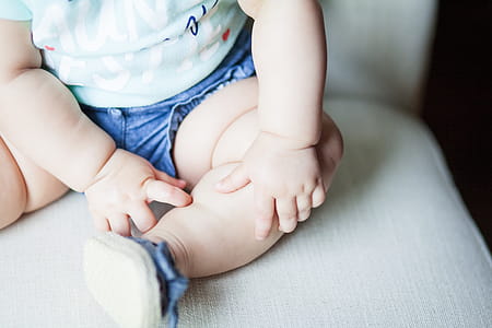 Baby Wearing Green Shirt and Blue Shorts Sitting on Gray Chair thumbnail