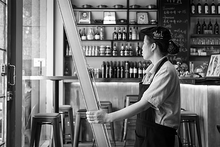 grayscale photography of woman wearing apron holding on gray metal bar thumbnail